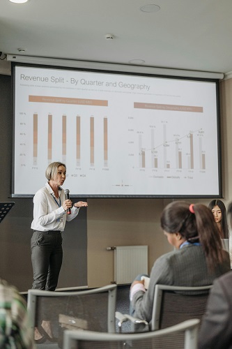 A confident speaker giving a presentation in front of an attentive audience, highlighting key visuals on a slide.