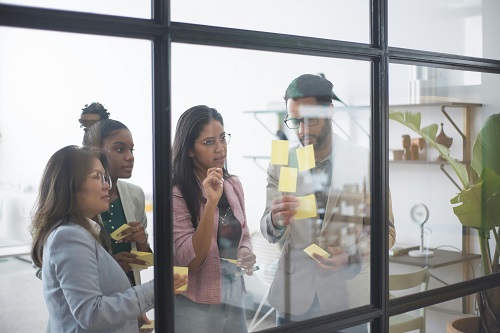 A diverse business team in a conference room brainstorming ideas for strategic planning on a glass wall.