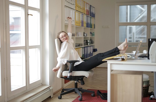 A person sitting on an office chair with their legs on the desk, stretching during a break to refresh and refocus.