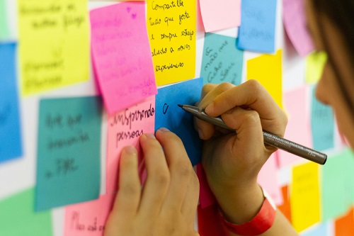 A person writing on a sticky note while standing in front of a board filled with colorful sticky notes, symbolizing organization and planning.