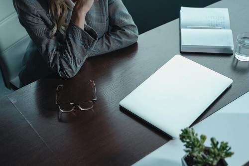 Business professional reflecting at a desk with a notepad and laptop, symbolizing overcoming tough times.