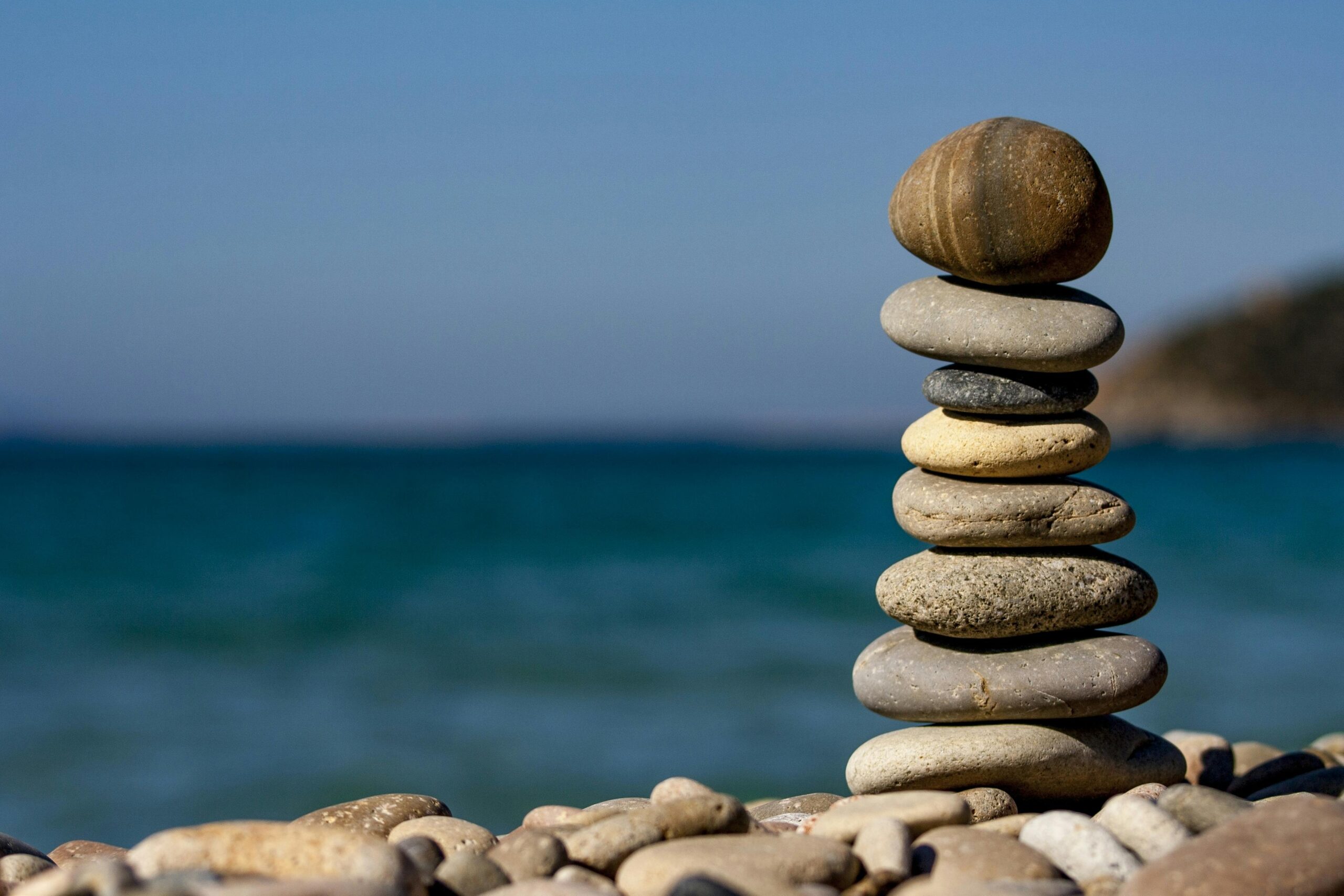 Small pebble stones on top of of each other next to a sea symbolizing balance.